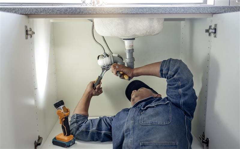 Plumber repairing pipes beneath a bathroom sink in Warrington