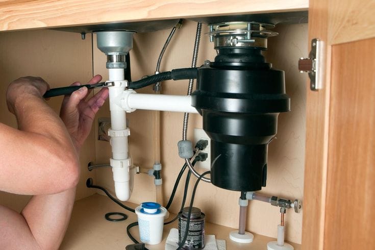 Plumber installing a garbage disposal beneath a kitchen sink in Warrington