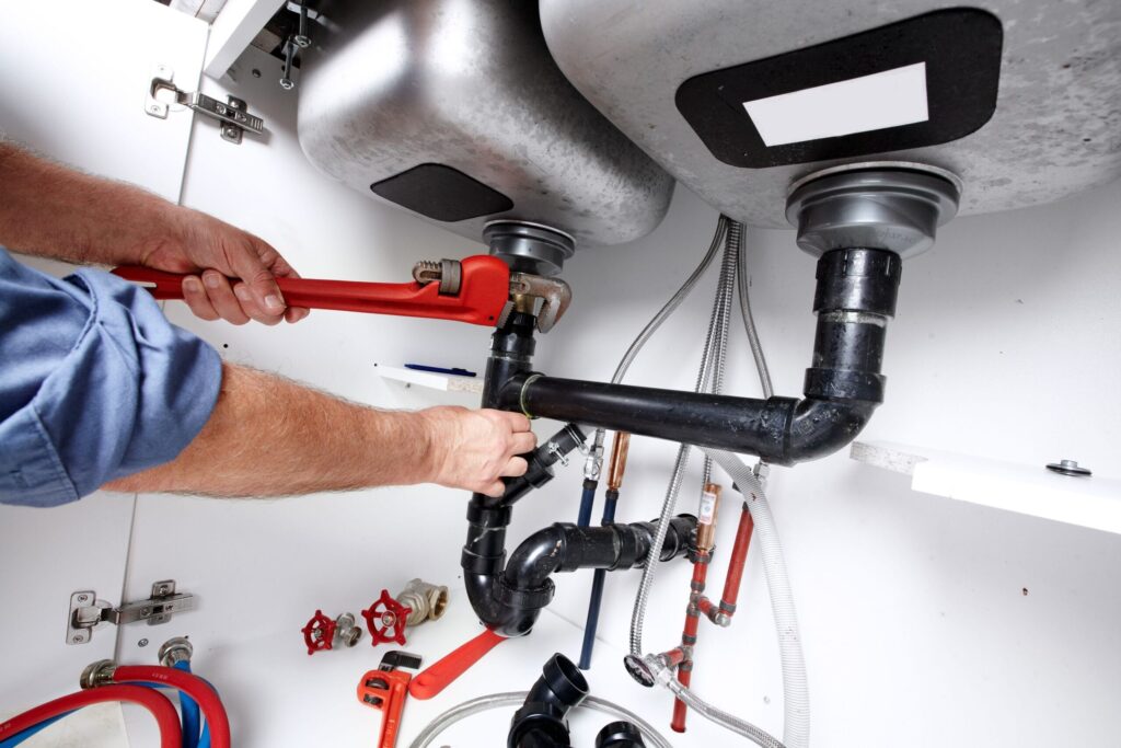 Plumber repairing drain pipes beneath a kitchen sink in Warrington