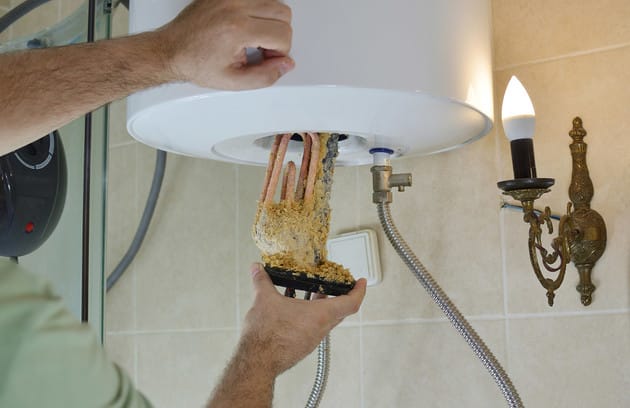 Technician removing mineral buildup from a water heater in Warrington